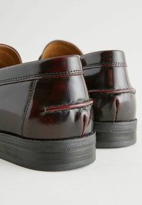 Zapatos de charol negros con un acabado brillante, que presentan acentos de costura, backs redondeados y una suela de goma plana.