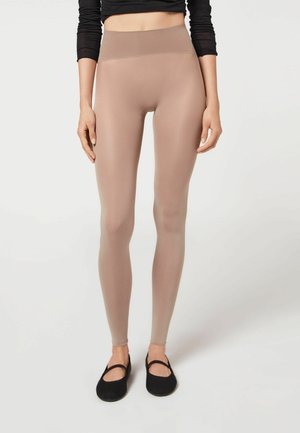Beige, hochgeschnittene Leggings aus glattem, dehnbarem Stoff, mit einem schlichten Design und passgenauem Sitz, kombiniert mit schwarzen Ballerinas.