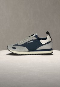 Χαμηλή αθλητική παπούτσια σε ναυτικό μπλε και γκρι με λευκές λεπτομέρειες, κορδόνια με σχέδια, και λογότυπο "ICEBERG" στο πλάι, εμφανίζεται σε ουδέτερη επιφάνεια.