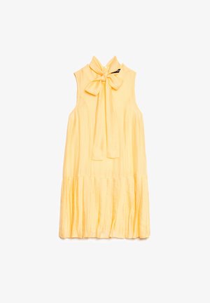 Käeauguta kollane kleit kõrge kaelusega, mis on seotud vööni ja volditud äärtega, asetatud lamedale valgele taustale.