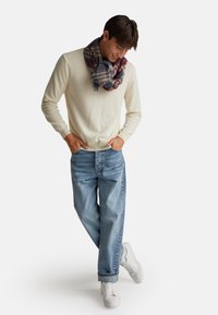 Crème gebreid sweater, lichtblauwe jeans en witte sneakers. Multicolore geruite sjaal om de hals gedrapeerd, casual snit en ontspannen silhouet.