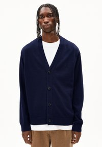 Cardigan bleu marine à boutons, fabriqué en tissu doux, avec un décolleté en V, des manches longues et un subtil motif tricoté sur les épaules.