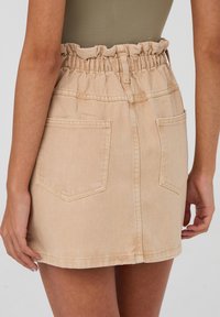 Gonna mini in denim beige con una vita elastica arricciata, due tasche posteriori e un orlo dritto. Senza chiusure o motivi visibili.