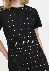 Black short-sleeve dress with silver studs arranged in a dotted pattern. Textured fabric with a fitted waist and smooth neckline.