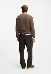 Maglione marrone lavorato a maglia con una vestibilità rilassata, abbinato a pantaloni scuri. L'outfit presenta una finitura testurizzata e un classico scollo a girocollo.