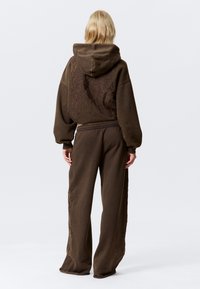 Bruine oversized hoodie en bijpassende brede sweatpants. Getextureerde stof met subtiele reliëfdesign op de rug en benen. Koordsluiting in de taille.