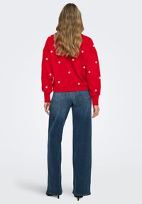 Red sweater with white embroidered flowers, paired with dark blue wide-leg jeans. Long sleeves gathered at cuffs, relaxed fit.