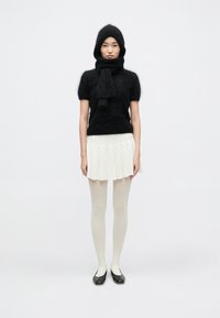 Top negru din tricotat pufos cu mâneci scurte, eșarfă asortată, fustă albă plisată, dresuri albe și pantofi negri comozi; design minimalist.