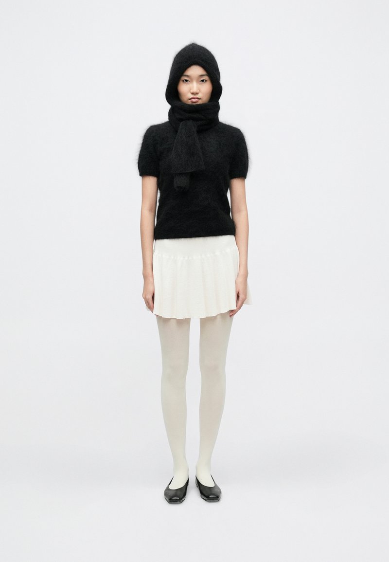 Top negru din tricotat pufos cu mâneci scurte, eșarfă asortată, fustă albă plisată, dresuri albe și pantofi negri comozi; design minimalist.