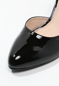 Chaussure à pointe noire en cuir verni, présentant une finition brillante, une texture lisse et un intérieur rembourré avec un revêtement beige.