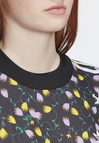 Černá květinová mikina s žlutými a fialovými květinovými vzory, žebrovaným černým límcem a měkkou texturou látky. Detail výstřihu a látky.