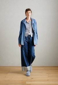 Denim jacket, gray shirt, wide-leg dark denim pants, and light blue shoes. Material textures are varied, with contrasting denim shades.