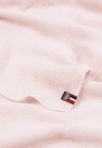 Tissu tricoté rose pâle avec une texture douce. Présente une petite étiquette avec un drapeau français et un logo sur un bord.