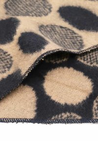 Coperta in lana beige con grandi motivi circolari neri. Il bordo presenta cuciture a contrasto in nero e una superficie morbida e texturizzata.