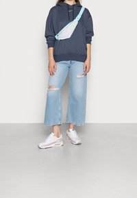 Sudadera navy con cordones, jeans de pierna ancha de lavado claro con dobladillos deshilachados y zapatillas blancas con detalles en rosa. Bolso cruzado en colores pastel.