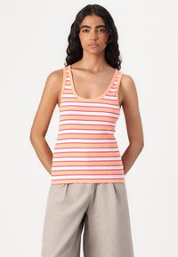 Striped tank top in peach with pink and white horizontal stripes, featuring a scoop neckline and ribbed texture. Paired with light gray pants.