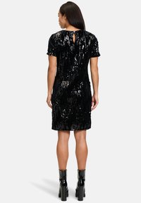 Czarna sukienka z cekinami, z krótkimi rękawami, do kolan, z wycięciem w kształcie łezki na plecach. Połączona z błyszczącymi czarnymi botkami na platformie.