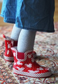Des bottes de pluie en caoutchouc rouge présentent des pois blancs et des motifs de souris, avec un accent rouge uni sur les côtés et une semelle texturée pour une meilleure adhérence.