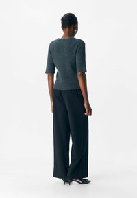 Gerippter, dunkelgrauer Pullover mit kurzen Ärmeln, tailliert in der Taille. Kombiniert mit locker sitzenden schwarzen Hosen und spitzen schwarzen Heels.