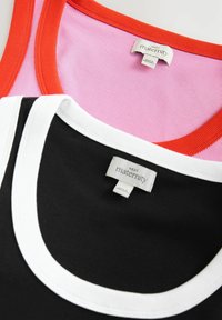 Zwarte top met witte rand en roze top met rode rand, met ribbeltextuur en labels die aangeven dat het van Next Maternity is.