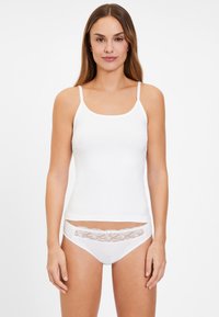 Weißes Baumwoll-Camisole mit dünnen Trägern, kombiniert mit weißen Panties, die am Bund mit floraler Spitze verziert sind. Hinweis auf eine glatte Textur und ein einfaches Design.