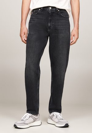 Jeans in denim nero con vestibilità dritta, dotati di cinque tasche, chiusura classica con bottone e leggere sfumature. Indossati con scarpe sportive grigie.