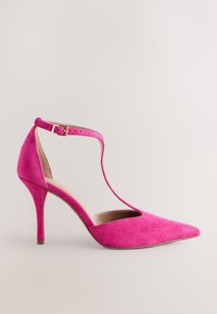 Rózsaszín velúrbőr magas sarkú cipő hegyes orral, bokapánttal és kivágásos mintával a lábfejnél. Vékony, tűsarkúval rendelkezik.