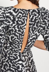 Černobíle vzorované šaty s výřezem na zádech, nabíranými rukávy a hladkým povrchem, s knoflíkovým zapínáním u krku.