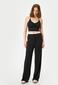 Sujetador deportivo negro corto con un frente fruncido, combinado con pantalones de chándal negros de corte holgado que cuentan con una cinturilla elástica blanca y cordón.