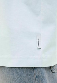 Helles, blaues Baumwoll-T-Shirt mit Seitenlabel, mit geradem Saum und glatter Textur, kombiniert mit hellen Jeansshorts.