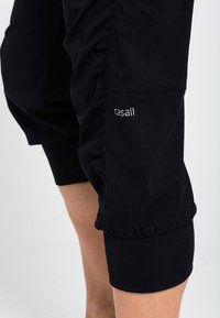 Černé sportovní šortky se sbíraným látkovým detailem na stehnech a přiléhavým lemem, s malým bílým logem "casall" na boku. Hladký povrch.