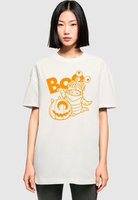 Hvid oversized t-shirt med et orange grafik af en tegneserie-frog, græskar og teksten "Boo." 100% bomuldsstof med en blød tekstur.