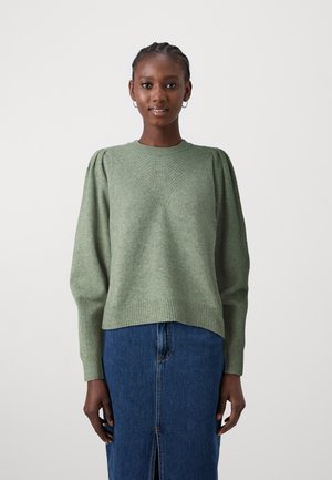 Green knitted sweater with puffed sleeves, textured diamond pattern on the front, ribbed cuffs, and hem. Paired with a denim skirt.