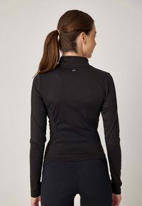 Czarna sportowa bluzka z długim rękawem o dopasowanym kroju, z wysokim kołnierzem i małym logo na plecach, wykonana z gładkiego, elastycznego materiału.