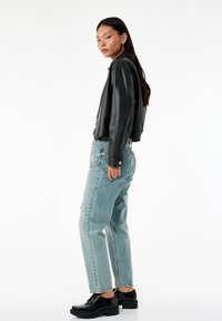 Chaqueta corta de cuero negro con textura suave, pantalones vaqueros de lavado claro con un ajuste holgado y zapatos de plataforma negros. Detalle de cadena plateada en los pantalones.