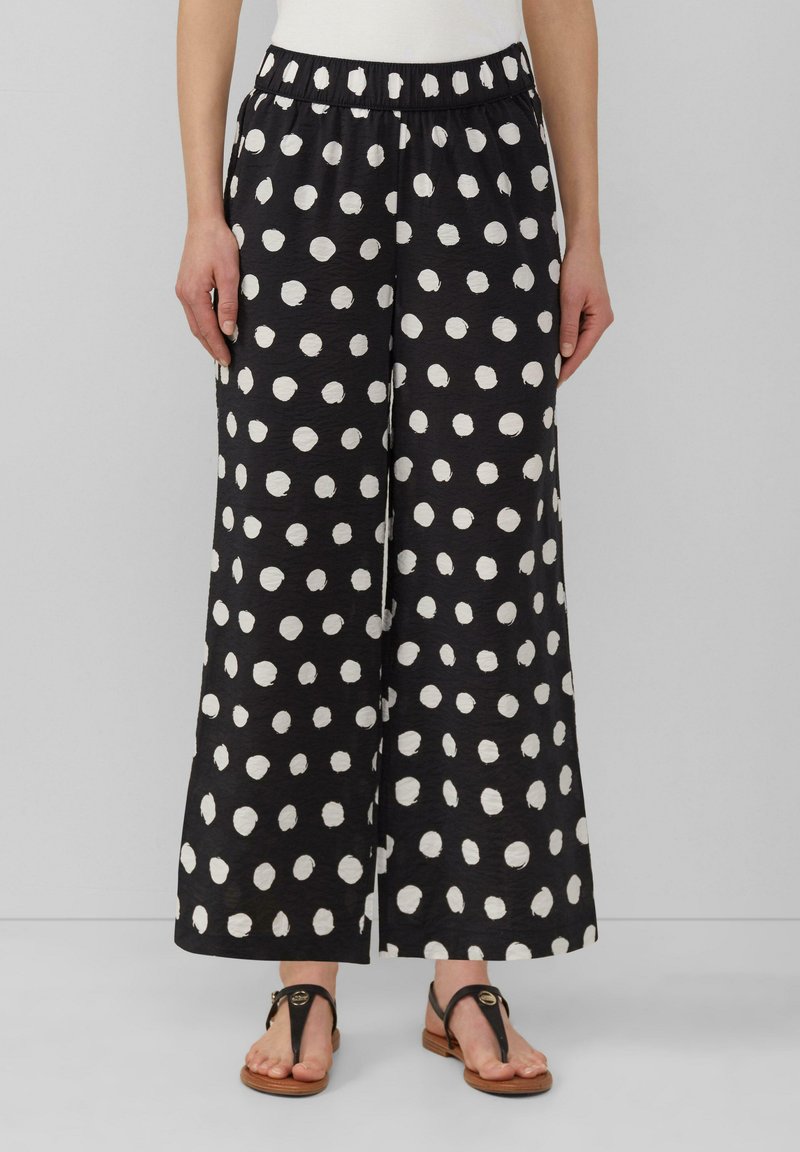 Culottes noirs avec de grands pois blancs, en tissu texturé. Dotés d'une taille élastique et de jambes larges et fluides.