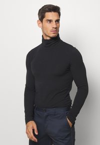 Camisa negra de manga larga tipo polo, confeccionada con tejido suave, diseño ajustado, con un cuello alto y agujeros para los pulgares, combinada con pantalones de rayas en color azul marino.