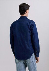 Cămașă din denim albastru închis, cu mâneci lungi și guler cu nasturi. Prezintă un spate drept și manșete cu nasturi, având o croială lejeră.