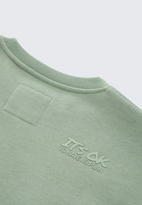Lichtgroene sweatshirt met geribde kraag, textiel met structuur, en geborduurde tekst "HET IS OKÉ OM GEEN PLAN TE HEBBEN" bij de hals.
