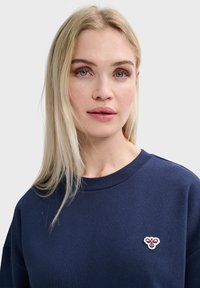 Donkerblauwe sweatshirt met een ronde halslijn, voorzien van een klein geborduurd bijenlogo op de linkerborst. Zachte stof, losse pasvorm.