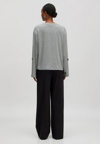 Grijze lange mouwen top met een relaxed fit en ronde hals, gecombineerd met zwarte wijde broek. Opvallende zwarte knoopaccenten op de mouwen.