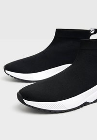 Sneakers neri slip-on in tessuto testurizzato, con suola in gomma bianca e dettagli a strisce sottili sui lati.