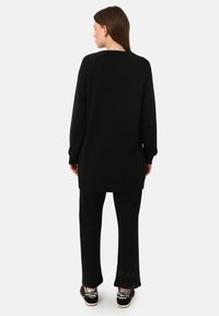 Sudadera negra de gran tamaño con mangas raglán, cuello redondo y dobladillo acanalado, combinada con pantalones negros a juego y zapatos negros con un patrón.