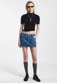 Sort kortærmet top, midtlængde blå denimnederdel, grå knæstrømper og sorte sneakers. Tilbehør inkluderer lagdelte halskæder og solbriller.