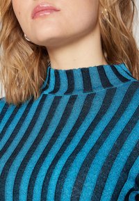 Svetr s vysokým stojáčkem v modro-černém pruhovaném designu, s ribbovanou strukturou, který vystihuje kontrastní vertikální pruhy a přiléhavý siluetu.