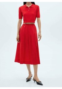Polo rojo corto con botones combinado con una falda roja plisada. El atuendo se completa con tacones slingback negros de punta.