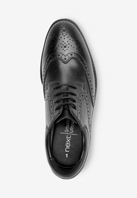 Chaussure habillée en cuir noir avec des détails en brogue, présentant une surface lisse, un bout arrondi et un système de laçage. Semelle intérieure Ortholite visible à l'intérieur.