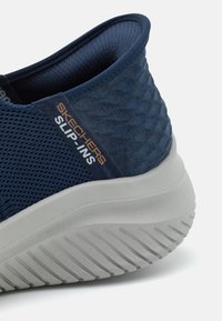 Marineblå mesh slip-on sneakers med en strukturert overdel, grå gummi såle og synlige mønstre på sålen. Har merkevaren på siden.