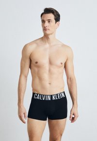 Schwarze Baumwoll-Boxershorts mit einem weißen "CALVIN KLEIN"-Logo am Bund, die eine enganliegende Passform und eine glatte Textur bieten.