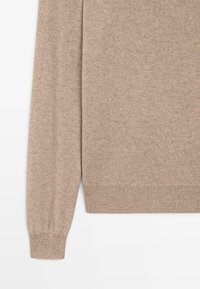 Beige stickad tröja med mjuk textur, med långa ärmar, ribbade muddar och rak nederkant. Inga synliga mönster eller metalldetaljer.